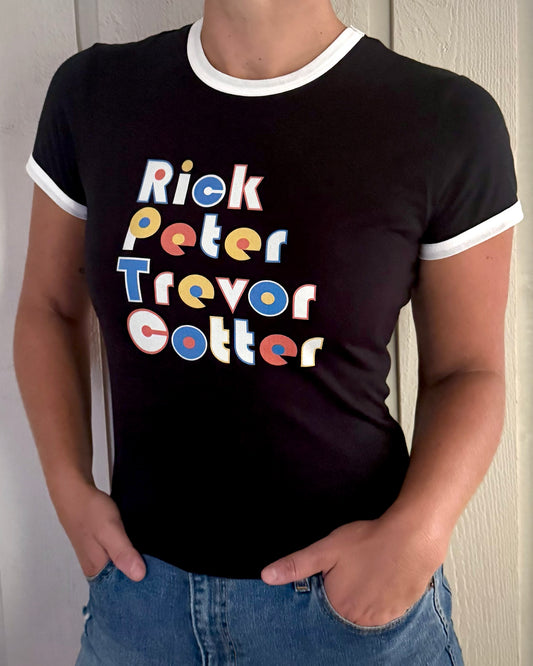 A person wearing a black ringer T-shirt with white trim and a colorful retro-style text graphic reading 'Rick Peter Trevor Cotter' on the front, paired with blue jeans against a light paneled wall.

Goose band womens merch t shirt dad funk peter trever cotter rick goose chicks